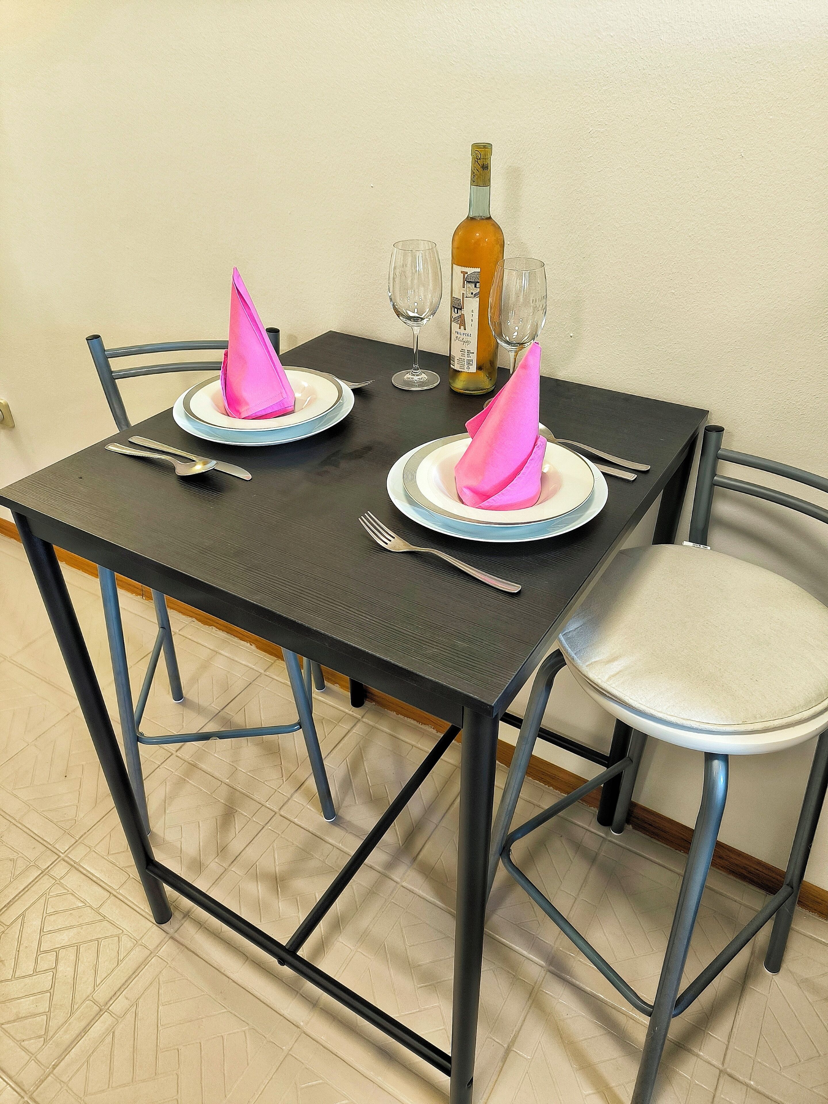 Una mesa de comedor preparada con platos, cubiertos y una botella de vino.