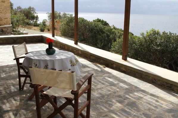 Una mesa con un florero de flores rojas, dos sillas de madera y vista al mar.