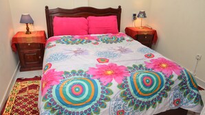 A bed with a colorful floral bedspread, two bedside tables with lamps, a red patterned rug, and a wooden headboard. - Cheap Accommodation in Marrakech (Marrakech)
