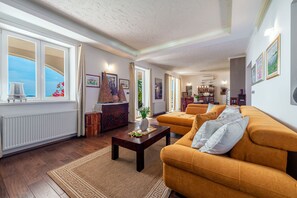 A spacious living room with a large window, a sofa, a coffee table, and a bookshelf.