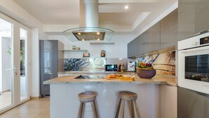 Een moderne keuken met een centraal eiland, barstoelen, roestvrijstalen apparatuur en een spatwand met een bloemenprint.