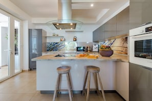 A modern kitchen with a central island, bar stools, stainless steel appliances, and a backsplash with a floral pattern.