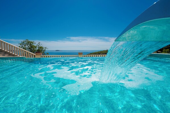 A swimming pool with clear water, a staircase, and a view of the ocean.