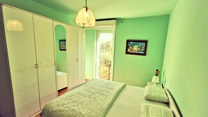 A bedroom with a bed, a wardrobe, a bedside table with a lamp, and a window with a view of the outdoors. - Holiday Apartment With a Balcony and sea View, Just 300 Metres From the Beach (Bol)