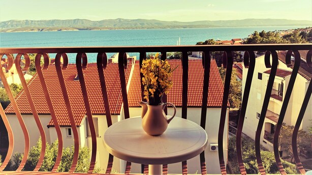 A balcony with a view of the sea and mountains, a white table with a vase of flowers, and red-tiled roofs. - Holiday Apartment With a Balcony and sea View, Just 300 Metres From the Beach (Bol)