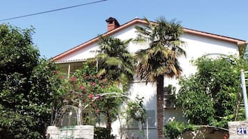 Un edificio blanco con techo rojo, pared de piedra y portón metálico.