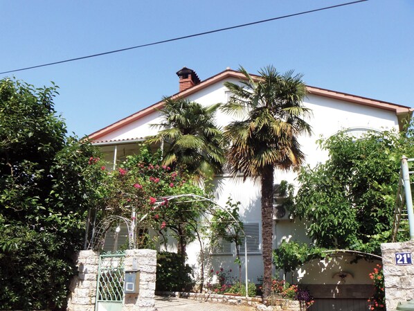 A white building with a red roof, a stone wall, and a metal gate.