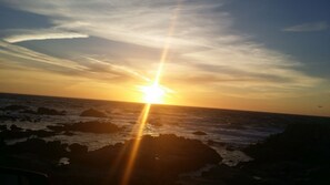 A sunset over a rocky coastline with the sun low on the horizon.