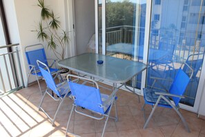 A balcony with a glass table and blue chairs, a potted plant, and a view of a balcony with chairs and a table. - Apartments 4 Dolphins Rogoznica (Rogoznica)