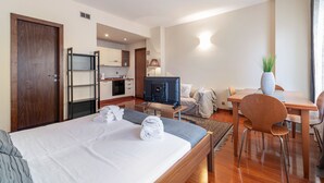 Een hotelkamer met een bed, een bureau, een televisie, een eettafel met stoelen, een kitchenette en een plant in een pot.