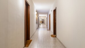 Een lange, smalle hotelgang met houten deuren aan beide kanten, een betegelde vloer en een lamp aan de linker muur.