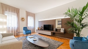 Una sala de estar moderna con un sofá, sillones, una mesita de centro, un televisor y una planta grande.