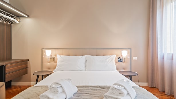 Una cama bien hecha con sábanas blancas, dos mesitas de noche con lámparas y una alfombra mullida.
