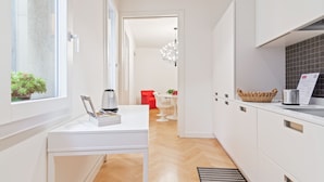 Una cocina moderna con armarios blancos, un comedor con una silla roja y vistas a otra habitación.