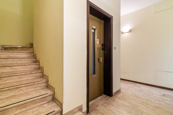 Una escalera que conduce a un ascensor en un edificio con paredes de color claro y suelo de baldosas.