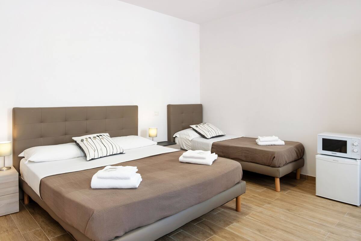 Een hotelkamer met twee bedden, een magnetron en een nachtkastje met een lamp.