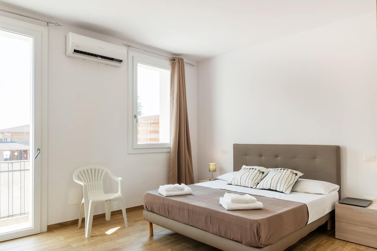 Een slaapkamer met een bed, een stoel, een nachtkastje en een airconditioning.
