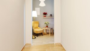 Een gang met een gele fauteuil, een klein tafeltje met een plant in pot, een witte engel decoratie, en een lamp.