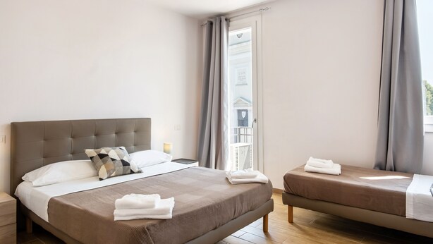 Een hotelkamer met een groot bed, een kleiner bed, een nachtkastje en een raam met gordijnen.