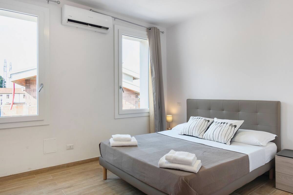 Een moderne slaapkamer met een groot bed, een nachtkastje en twee ramen.