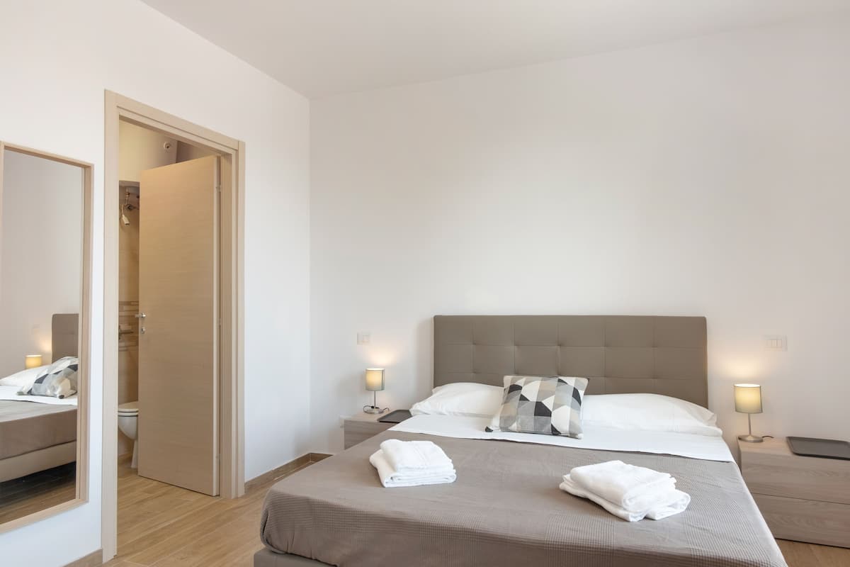 Een moderne hotelkamer met een groot bed, bedlampen, een spiegel en een houten vloer.