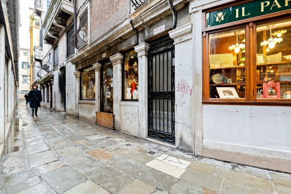 A narrow street with stone pavement, a shop with a sign reading "IL PAP", and a person walking away. - Ponte di Rialto Penthouse with Panoramic Terrace (Venice)