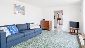 Un salon avec un canapé bleu, une commode en bois et un téléviseur posé sur un meuble en bois.