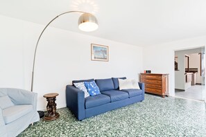 A living room with a blue sofa, a small round table, a floor lamp, and a wooden dresser. - Ponte di Rialto Penthouse with Panoramic Terrace (Venice)