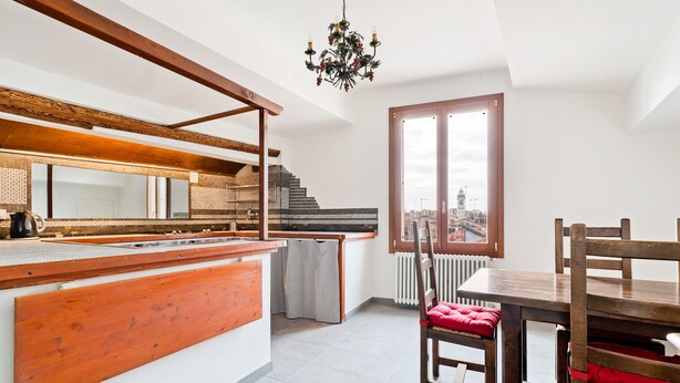 Une cuisine moderne avec un îlot central en bois, un coin repas avec une table et des chaises, et une vue sur la ville grâce à une grande fenêtre.