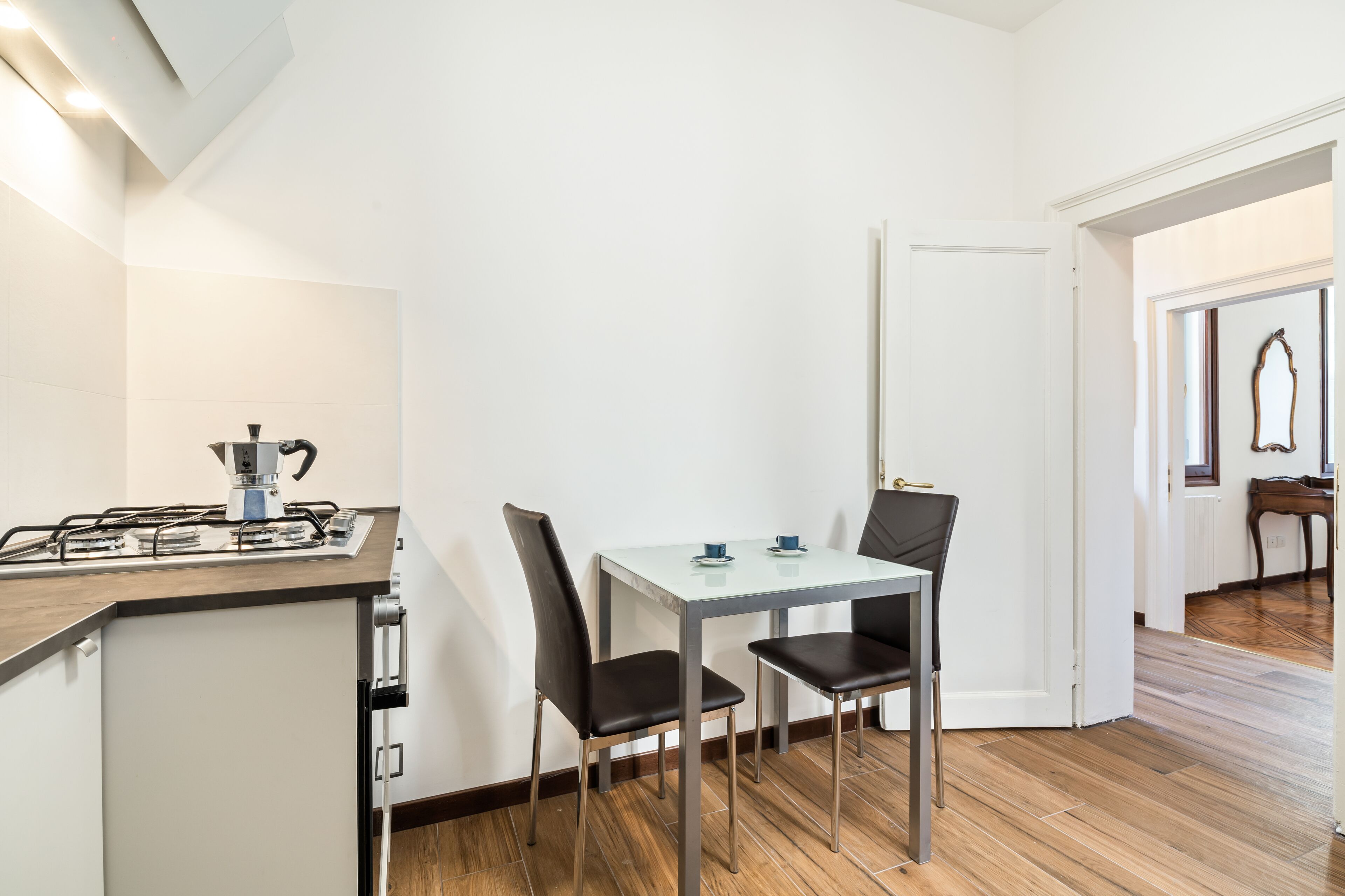 Una cocina compacta con estufa a gas, dos sillas y una mesa pequeña.