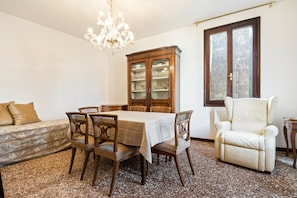 Un coin repas avec une table dressée pour quatre personnes, entourée de chaises en bois. On aperçoit un meuble avec des portes en verre à l’arrière-plan.