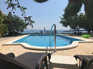 A swimming pool with a metal ladder, surrounded by stone tiles, with lounge chairs and a view of the sea. - House With Pool in Split Near the Beach (Split)
