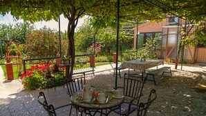 Un patio con mesa y sillas redondas, rodeado de un jardín de flores rojas y un muro de ladrillo.