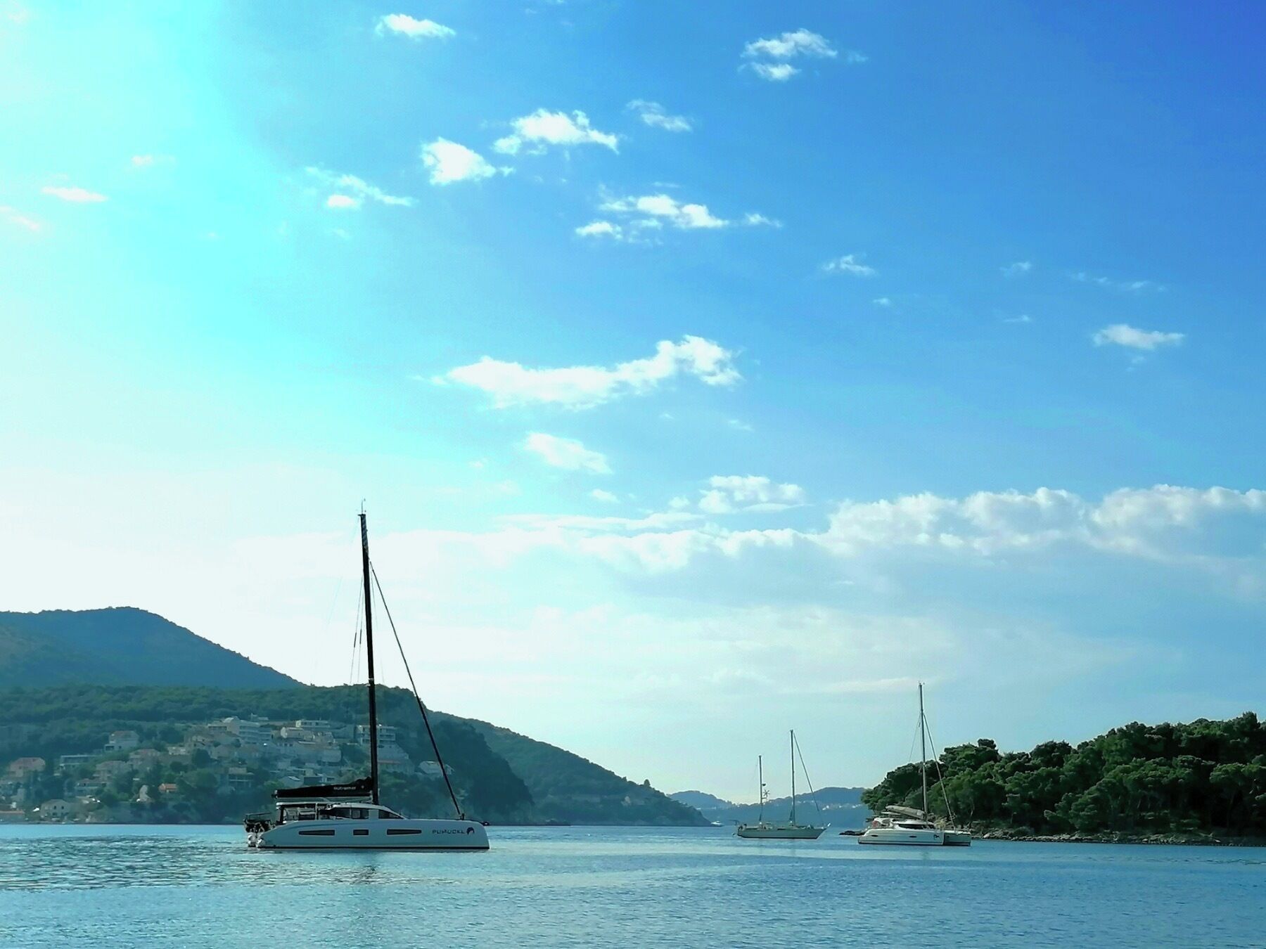 Un’acqua calma con barche a vela, montagne sullo sfondo e cielo sereno.