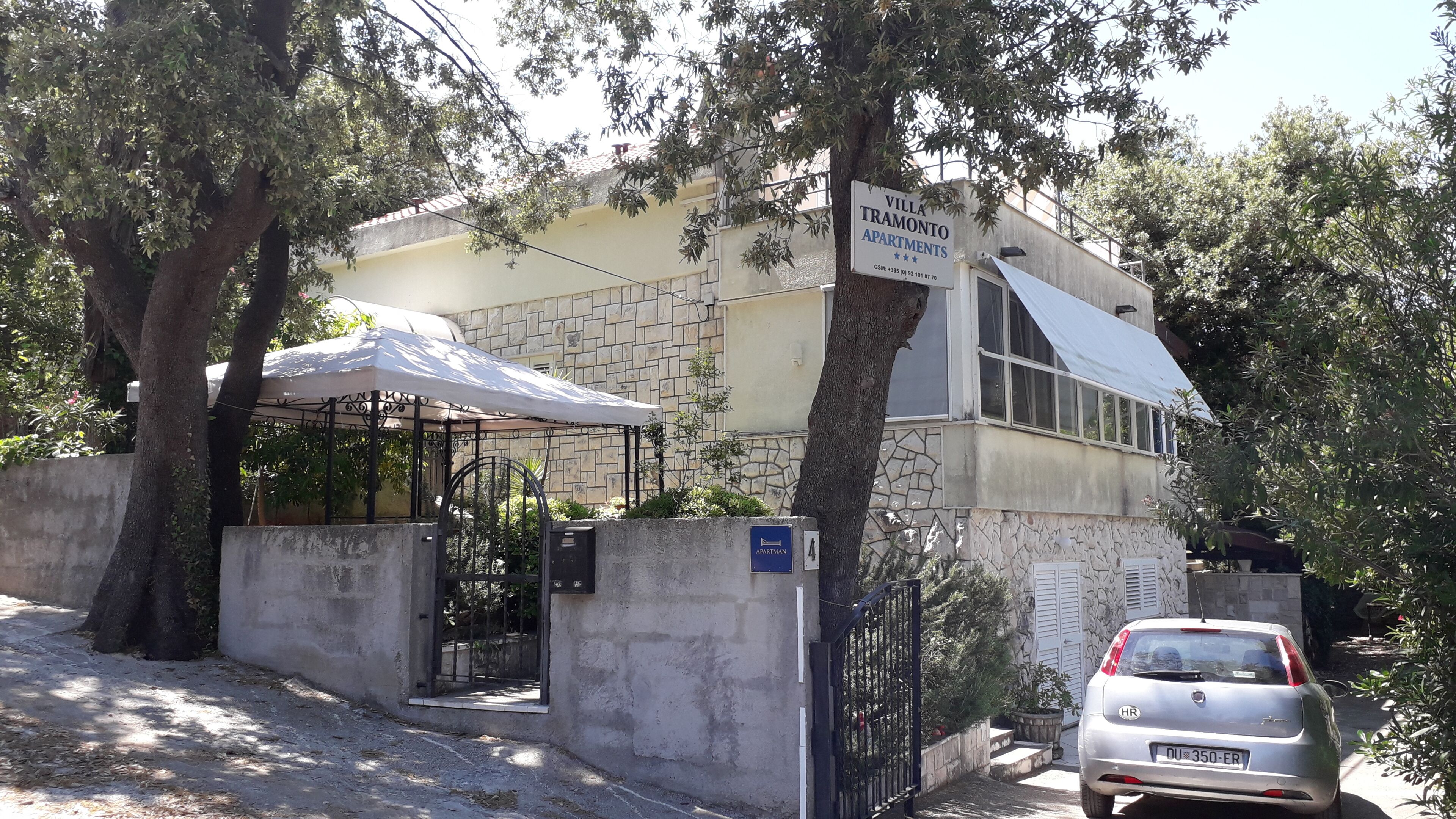 Apartamentos Villa Ramonto con entrada protegida por un portón, zona de estar exterior cubierta y un coche estacionado.