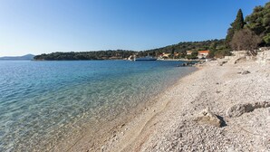 A pebble beach with clear water, a boat, and buildings in the background. - Room-the Most Beautiful Position in Zato (Dubrovnik)