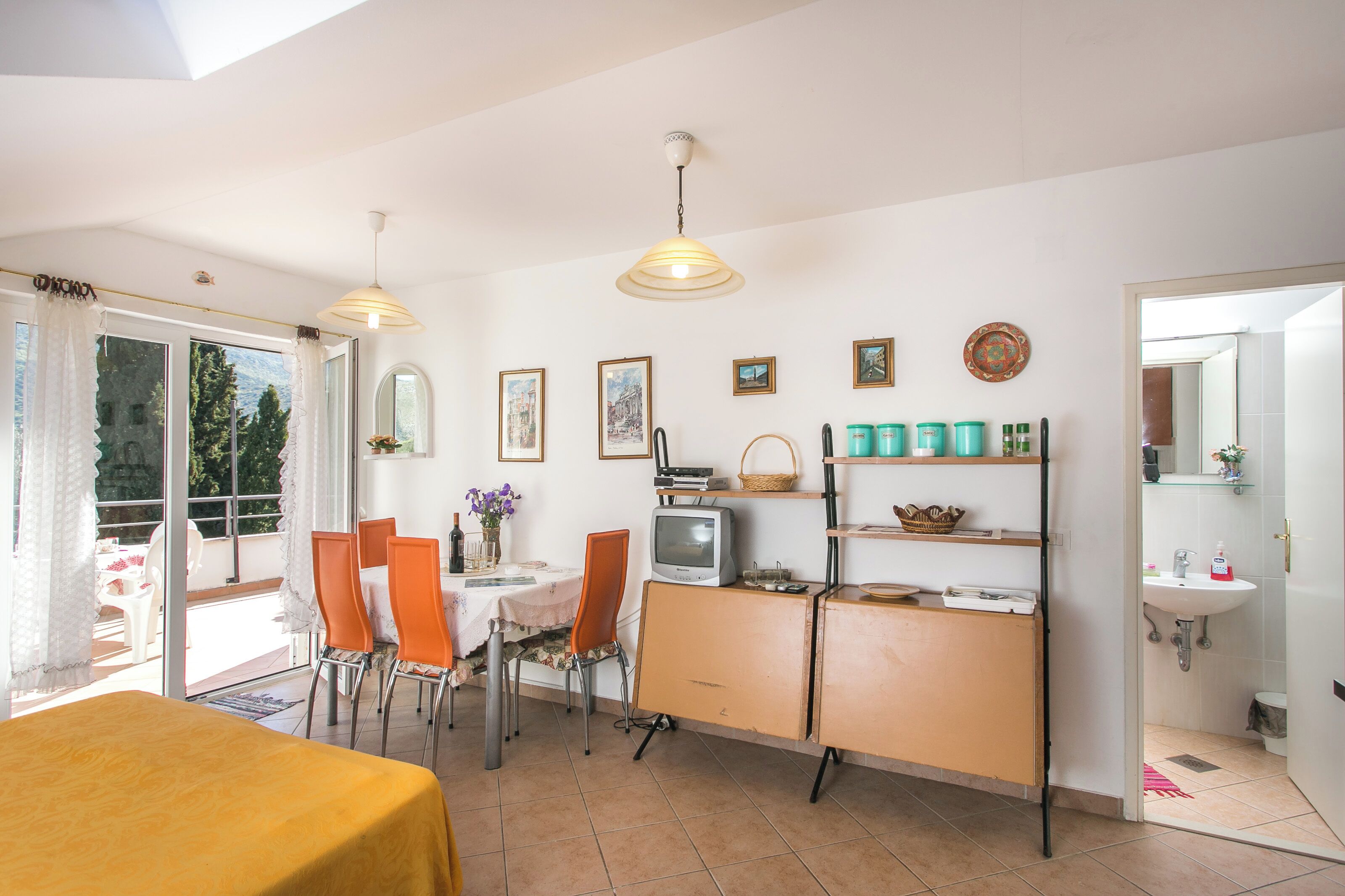 A dining area with a table, chairs, a television, and a kitchen area with shelves and a sink.