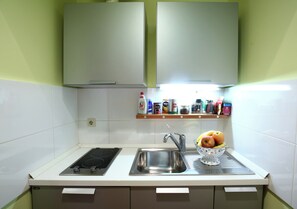 Uma cozinha com fogão, pia e uma tigela de frutas no balcão.