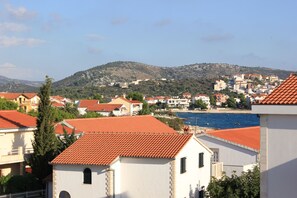 Une ville côtière aux toits recouverts de tuiles rouges, aux bâtiments blancs, et qui offre une vue sur la mer et les collines en arrière-plan.