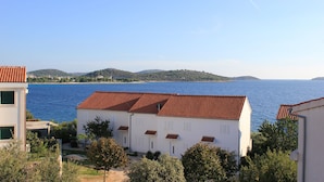 Un bâtiment situé sur la côte, doté d’un toit recouvert de tuiles rouges, de murs blancs et offrant une vue sur la mer et les collines en arrière-plan.
