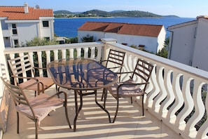 Un balcon avec une table en verre et quatre chaises, donnant sur une étendue d’eau et des collines.
