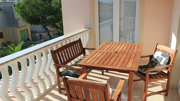 A balcony with a wooden table and chairs, a white railing, and a view of buildings and trees. - Welcome to Apartments 4 Dolphins, Rogoznica, Croatia (Rogoznica)