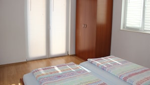 A bedroom with a wooden wardrobe, a bed with patterned bedding, and a window with blinds. - Welcome to Apartments 4 Dolphins, Rogoznica, Croatia (Rogoznica)