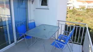 Ein Balkon mit Glastisch und blauen Stühlen, einer Schiebeglastür und Blick auf eine Hügelkuppe mit Gebäuden.