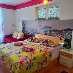 A bedroom with a cityscape mural, a bed with floral bedding, a red sofa, and a nightstand with a plant. - Pretty Apartment With Terrace on Island Rab (Rab)