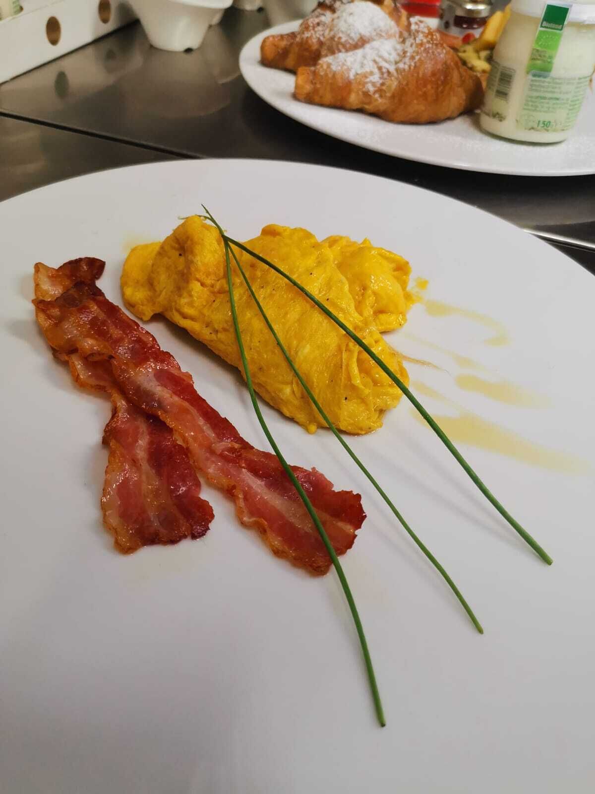 Un plato con huevos revueltos, tocino y cebollín sobre un plato blanco.