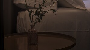 Una camera da letto con un letto, un comodino con un vaso di fiori, un tavolo rotondo e una finestra vista verde.