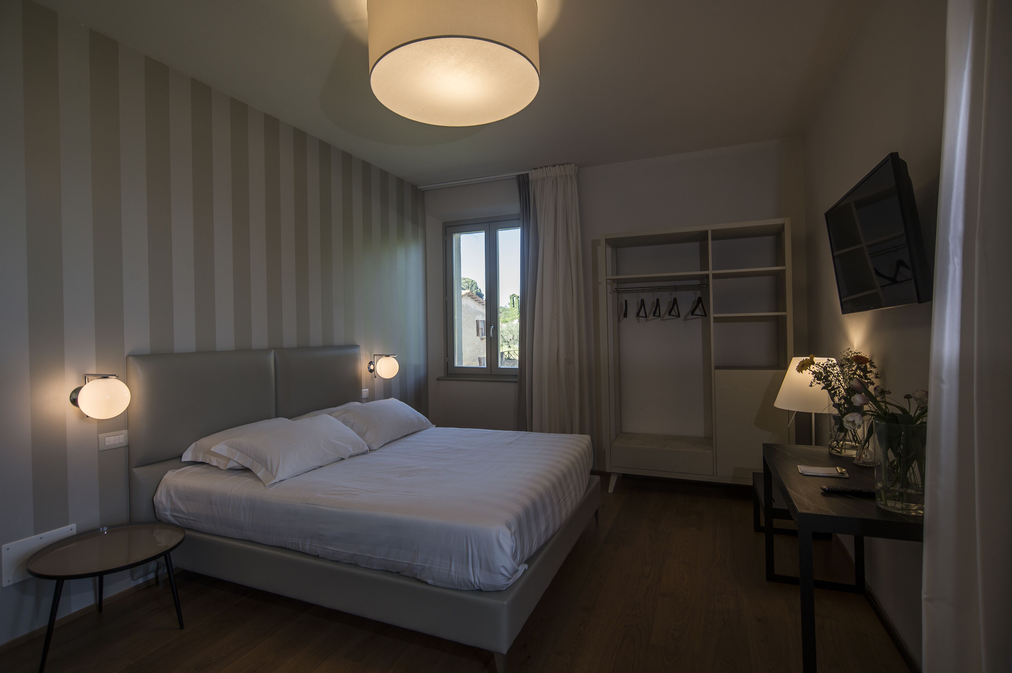A bedroom with a bed, bedside tables, a desk, a chair, a wardrobe, and a TV mounted on the wall.