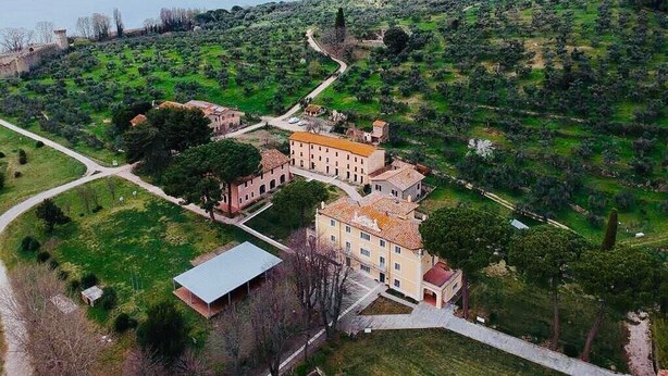 Vista aerea di una storica tenuta con un edificio principale, una struttura fortificata e un sentiero che conduce al mare.