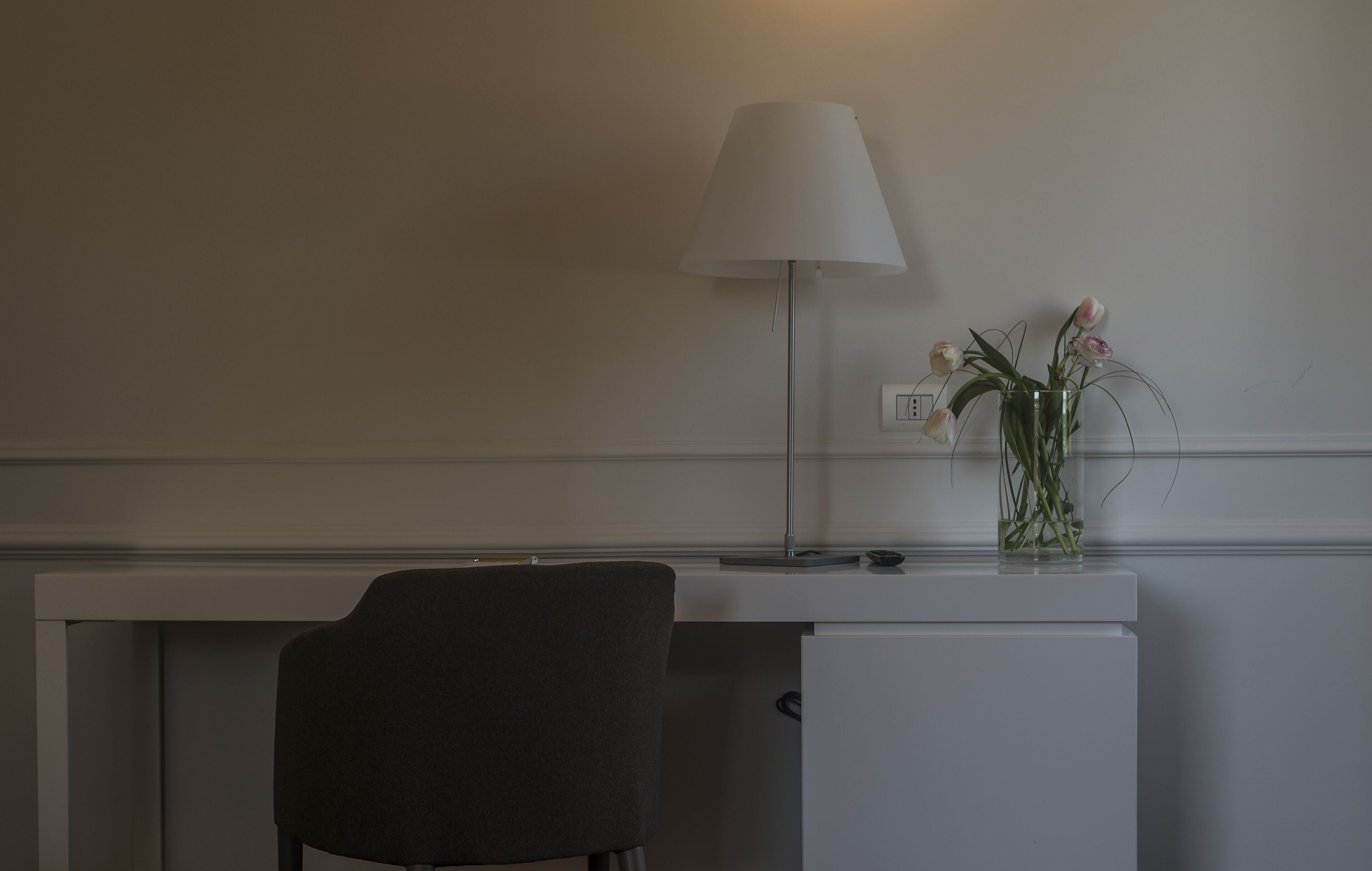 A desk with a lamp, a chair, and a vase with flowers.
